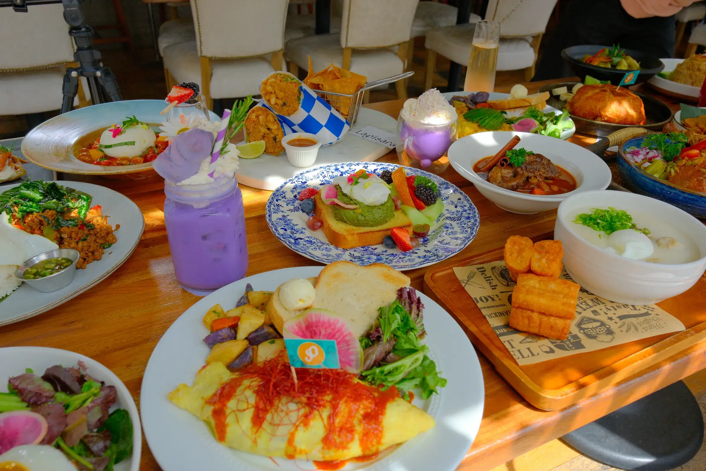 A table of brunch plates with an omelette, spring rolls and a purple iced drink